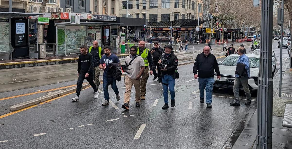 Security guard Daniel Jones (in the bright fluro vest in the centre) standing behind online commentator, Avi Yemini, and videographer, Rukshan Fernando, in Melbourne, Australia. (Josh Spasaro/The Epoch Times).