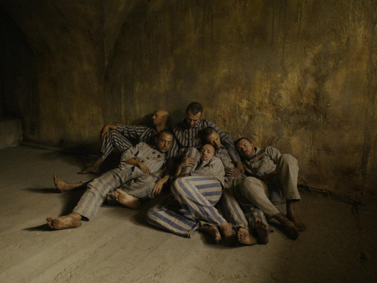 The men imprisoned in a cell at Auschwitz gather around Father Maximilian Kolbe (Marcin Kwasny), in “Triumph of the Heart.” (Sherwood Fellows)
