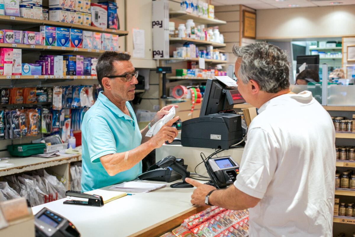 A sales clerk helps a man with his prescription drugs at a pharmacy in New York City on June 18, 2014. (Benjamin Chasteen/The Epoch Times)