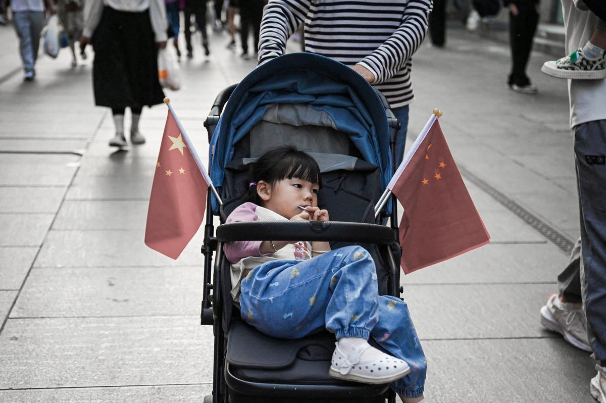 2023年5月3日,一名兒童坐在裝飾著中國國旗的嬰兒車裏,母親推著她穿過北京前門大街。根據聯合國人口司的數據,到2023年,中國的生育率已降至每名婦女生育不到一個孩子。(Greg Baker/AFP via Getty Images)