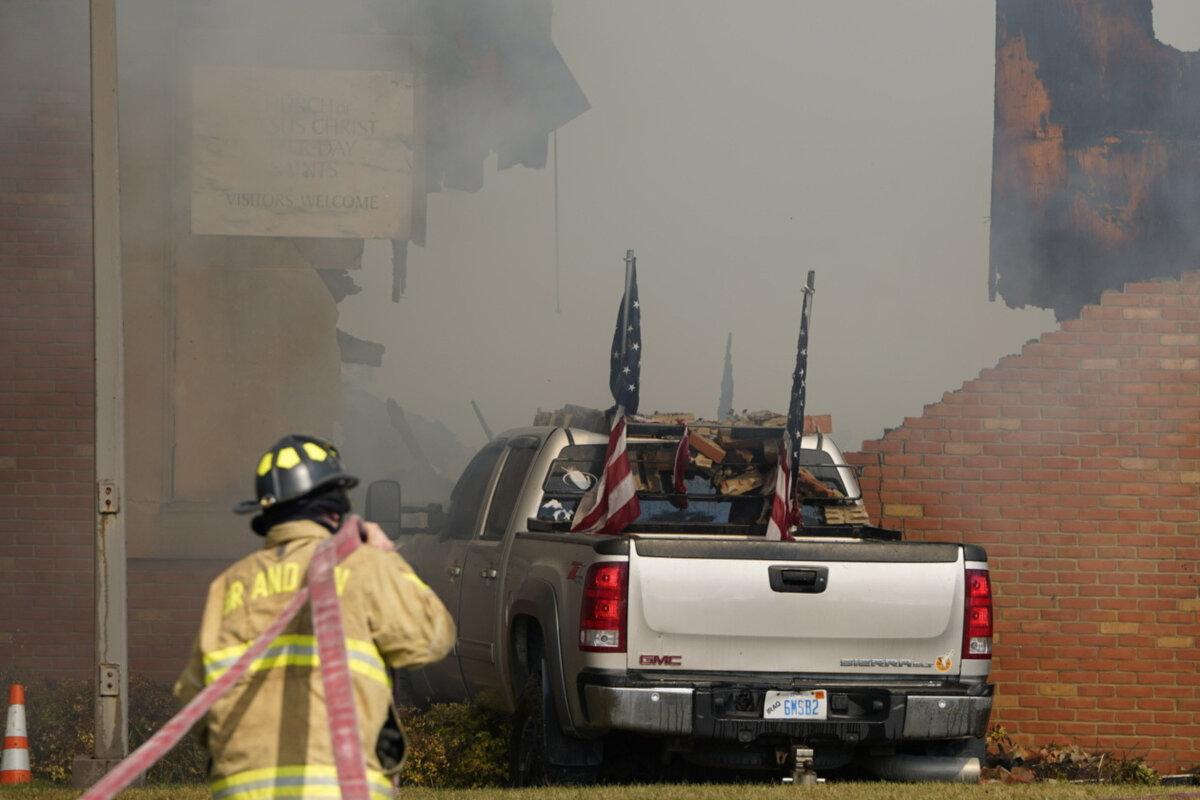 A vehicle that was rammed into the building is surrounded by smoke as a firefighter works on the scene at the Church of Jesus Christ of Latter-day Saints in Grand Blanc, Mich., on Sept. 28, 2025. (Lukas Katilius/The Flint Journal via AP)