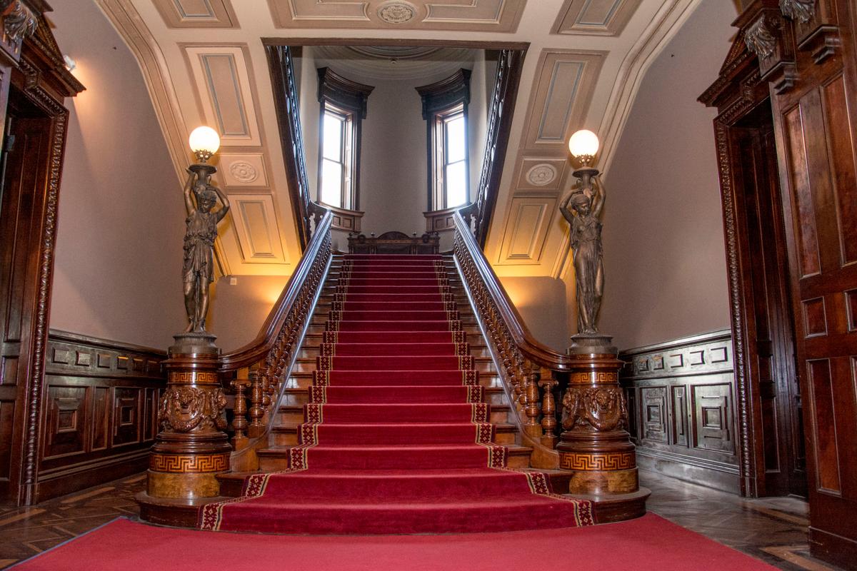 The Grand Staircase, which dominates the north side of the rotunda, was designed by the Herter Brothers firm in New York City. Made primarily of black walnut inlaid with satinwood, the imperial staircase features newel posts that are carved with lion heads and garlands. The rails and balusters are inlaid with boxwood and feature a Greek key and palmette pattern. (<a href="https://www.sarahgroteart.com/" target="_blank" rel="nofollow noopener">Sarah Grote Photography</a>/Lockwood-Mathews Mansion Museum)