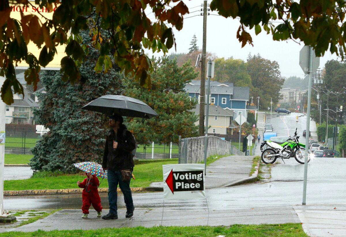 Rain falls as a man and child make their way to a school serving as a voting station in Esquimalt, B.C., on Oct. 19, 2024. (The Canadian Press/Chad Hipolito)