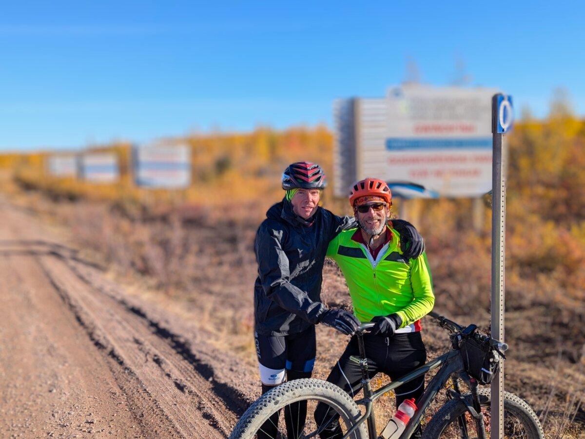 Lloyd Taylor (L) and teammate Steve Iseman pose at the end of the Dempster Highway in Inuvik on the northern leg of the Spinning Wheels Tour before heading to Tuktoyaktuk on the Inuvik Tuktoyaktuk Highway, in September 2024. (Courtesy Spinning Wheels Tour)