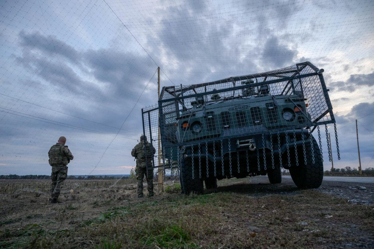 Ukrainian soldiers stand beside an armoured military vehicle surrounded by a cage to protect against drone attacks on a road near Oleksandrivka, Ukraine, on Oct. 6, 2025. (Ed Jones/AFP via Getty Images)