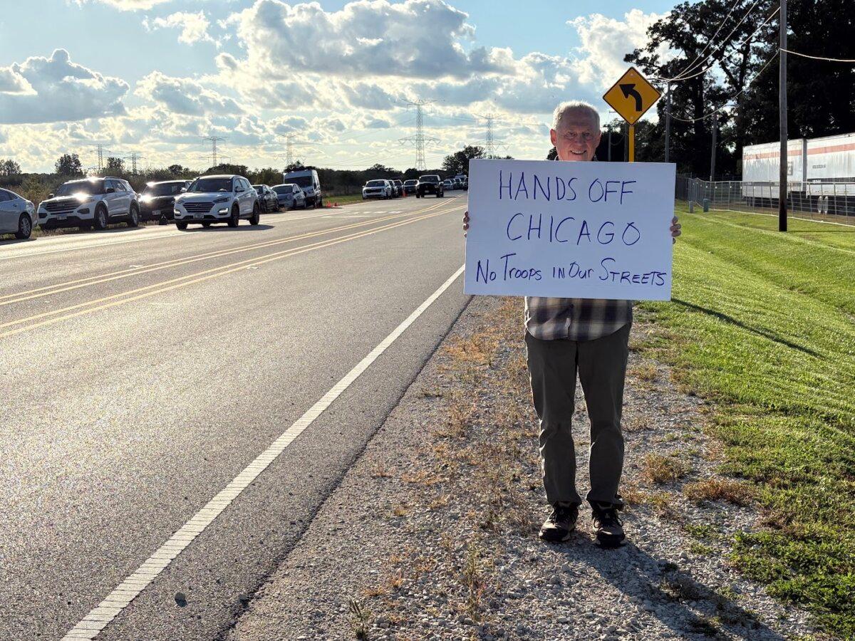 A protester holds a sign outside an Army Reserve Training Center in Elwood, Ill. on Oct. 7, 2025. (Nathan Worcester/The Epoch Times)