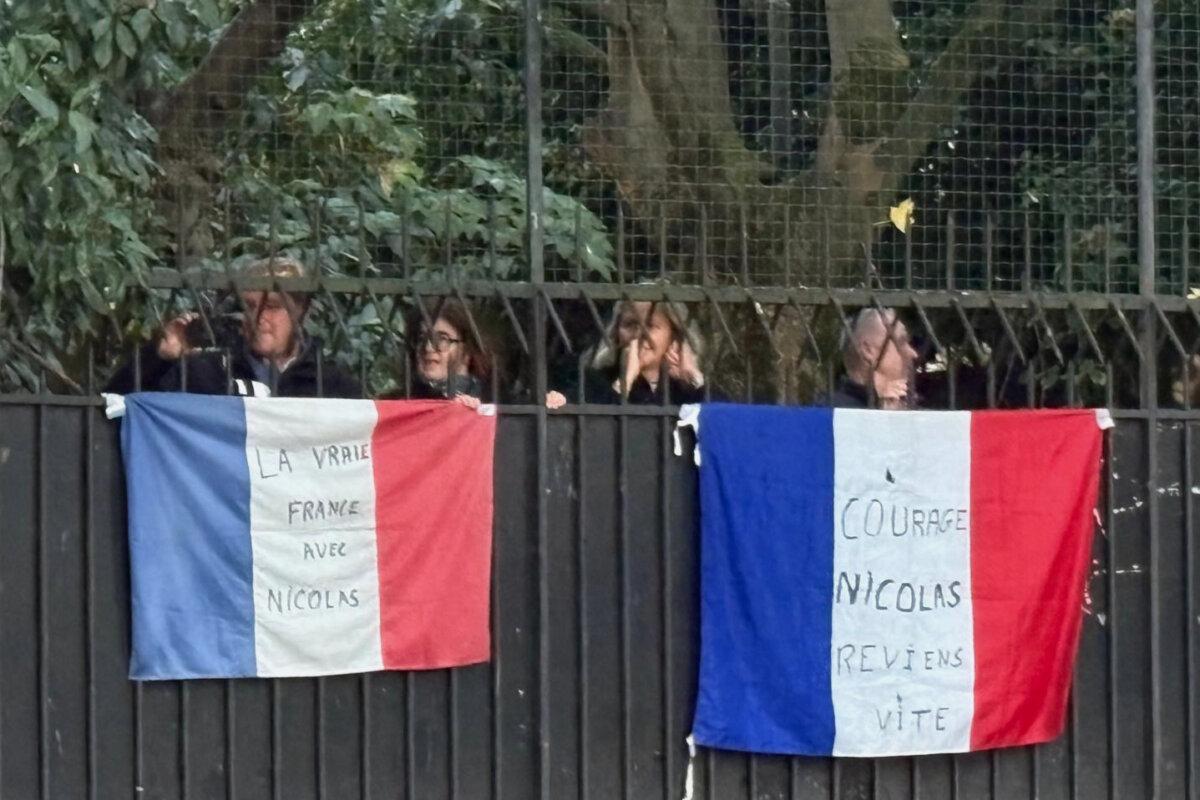 People stand behind French flags with an inscription reading "Courage Nicolas, come back soon," and another reading, "True France with Nicolas," outside former French President Nicolas Sarkozy's home in Paris on Oct. 21, 2025. (AP Photo/Masha Macpherson)