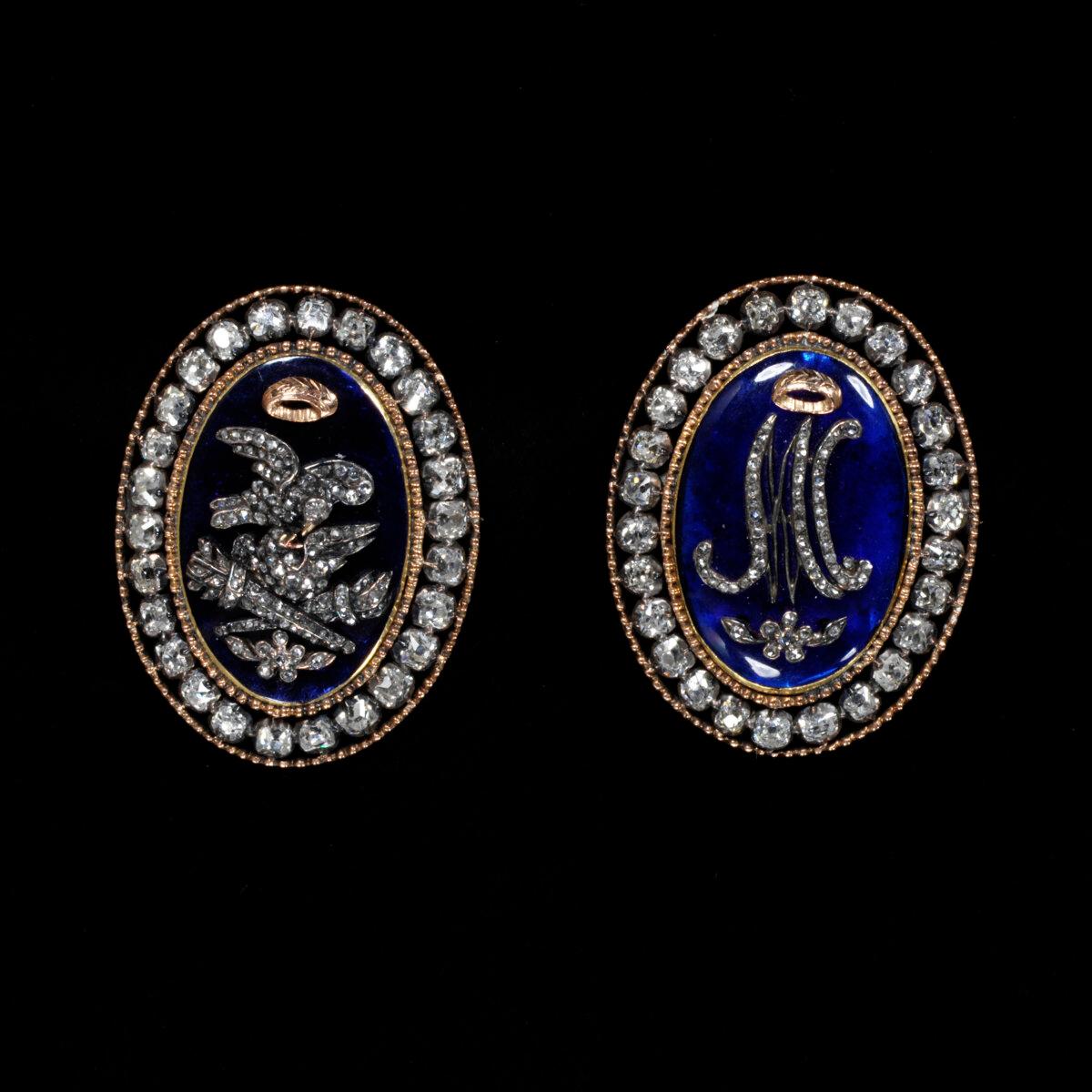 A pair of neoclassical-style braided bracelet clasps, circa 1770. (L) Plaque is decorated with turtle doves and hymeneal torches, and (R) plaque is adorned with Marie Antoinette’s monogram. Gold with brilliant-cut diamonds with central plaques of blue paste (glass). (Copyright Victoria and Albert Museum, London)