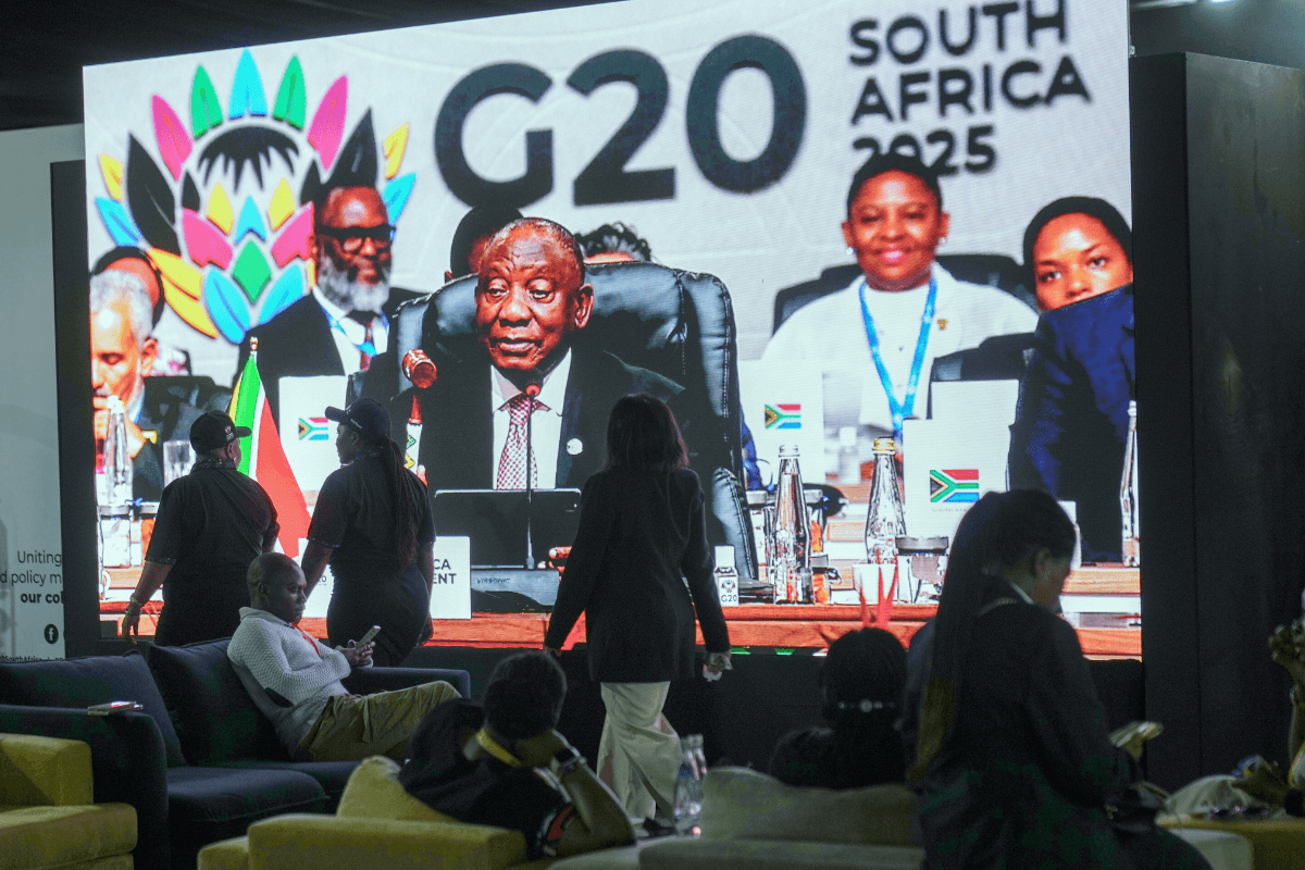 People walk by a large screen TV where South African President Cyril Ramaphosa holds a wooden gavel as he officially closes the G20 leaders' summit, in Johannesburg, on Nov. 23, 2025. (Jerome Delay/AP Photo)