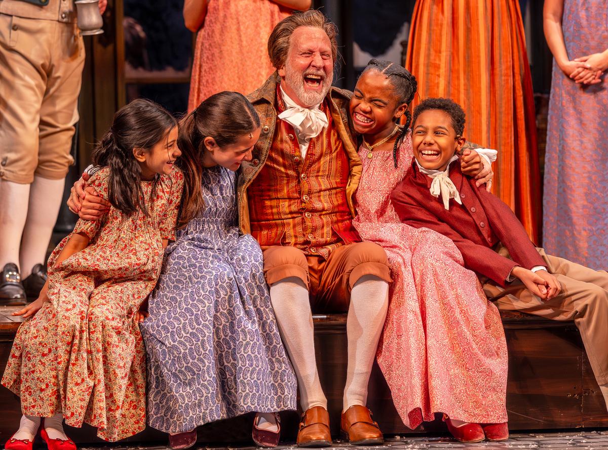 (L–R) Tiny Tim (Ella Boparai), Belinda Cratchit (Viva Boresi), Mr. Fezziwig (Robert Schleifer), Emily Cratchit (A'mia Imani), and Gregory Cratchit (Carmelo Kelly), in "A Christmas Carol." (Brett Beiner)
