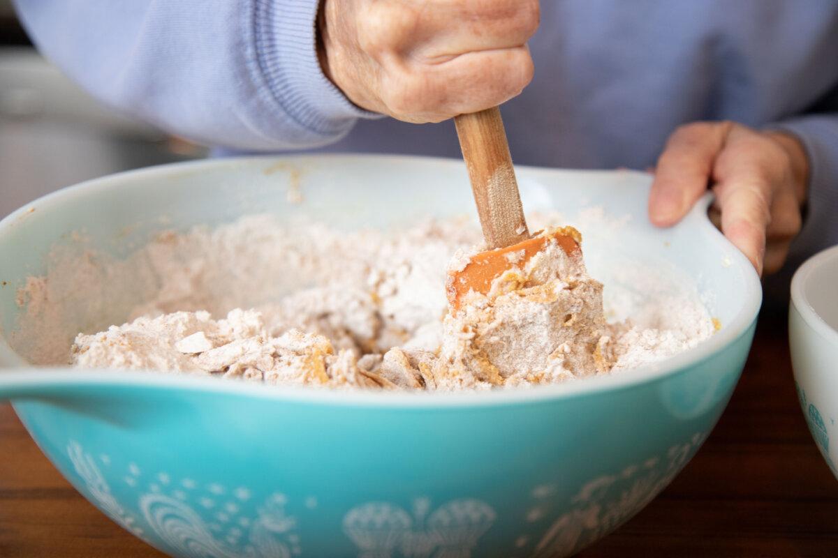A senior woman standing in a kitchen mixing cookie dough in a bowl with a spatula. (Meaghanbrowning/Getty Images)