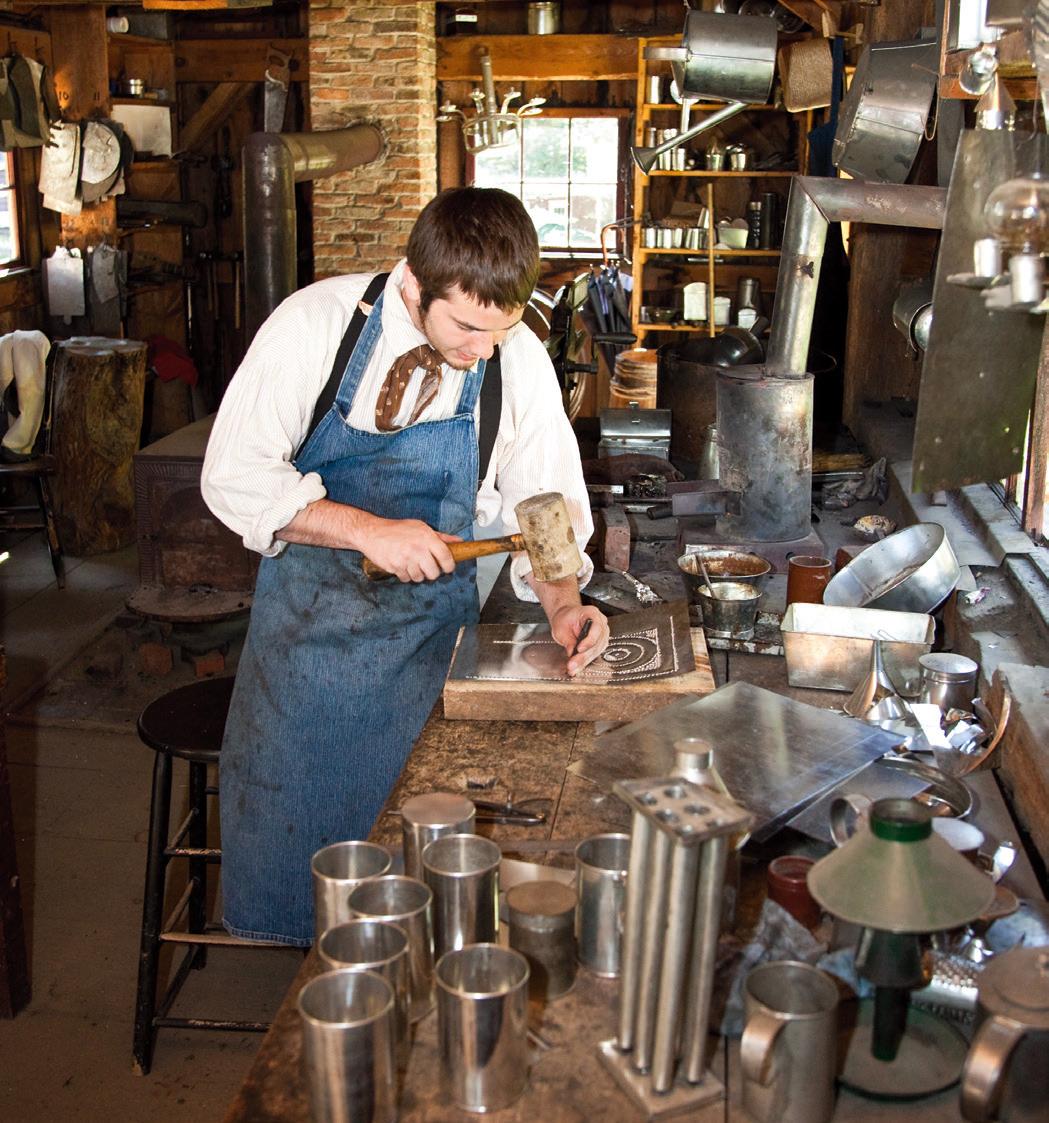 A costumed interpreter punches tin for a lamp in the Tin Shop at Old Sturbridge Village, Mass. (Jeff Schultes/Shutterstock)