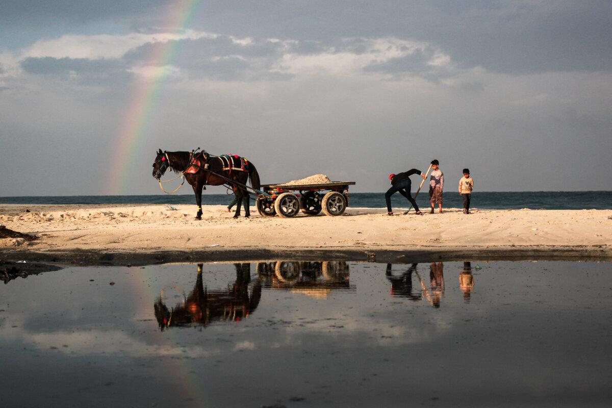 A man loads a horse cart with sand as a rainbow emerges over Deir al-Balah, in the central Gaza Strip, on December 10, 2025. (Bashar Taleb/AFP via Getty Images)