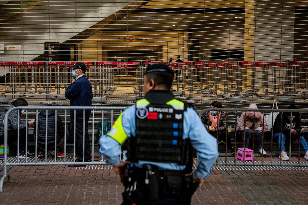 A police officer keeps watch as people wait in line to enter the West Kowloon Law Courts building to hear the verdicts in the national security trial of pro-democracy media tycoon Jimmy Lai in Hong Kong on Dec. 15, 2025. (Leung Man Hei/AFP via Getty Images)