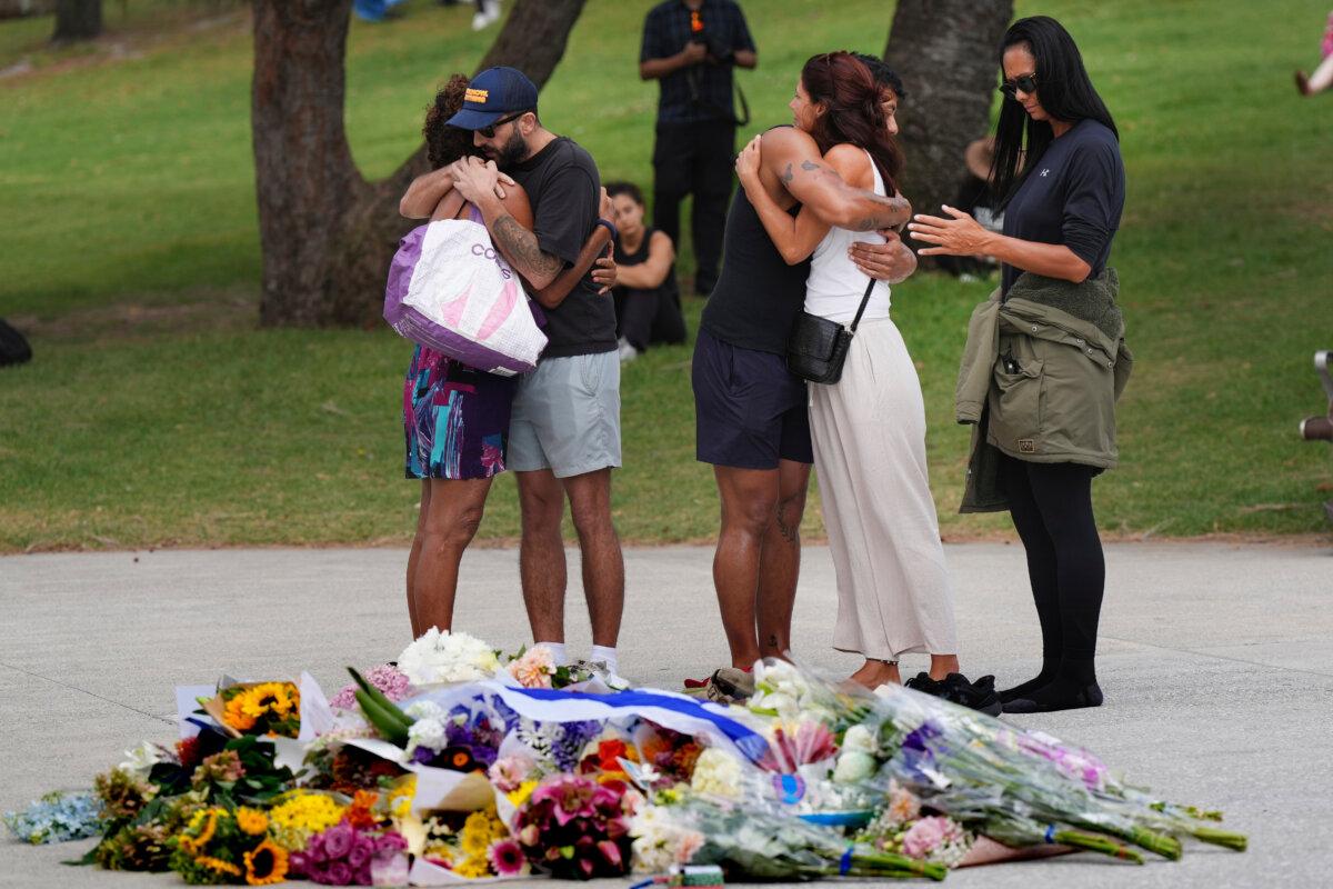 People embrace at a flower memorial placed outside Bondi Pavilion at Sydney's Bondi Beach, on Dec. 15, 2025, a day after two gunmen opened fire during a Hanukkah celebration. (AP Photo/Mark Baker)