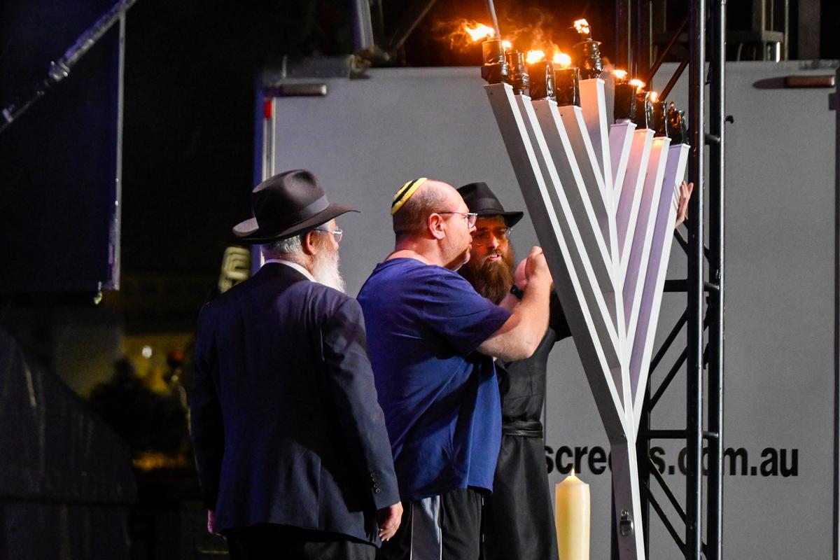 The father (2nd of L) of 10-year-old victim Matilda, greeted on stage as he lights the eighth candle of a menorah in Sydney, Australia, on Dec. 21, 2025. (Saeed Khan/AFP via Getty Images)