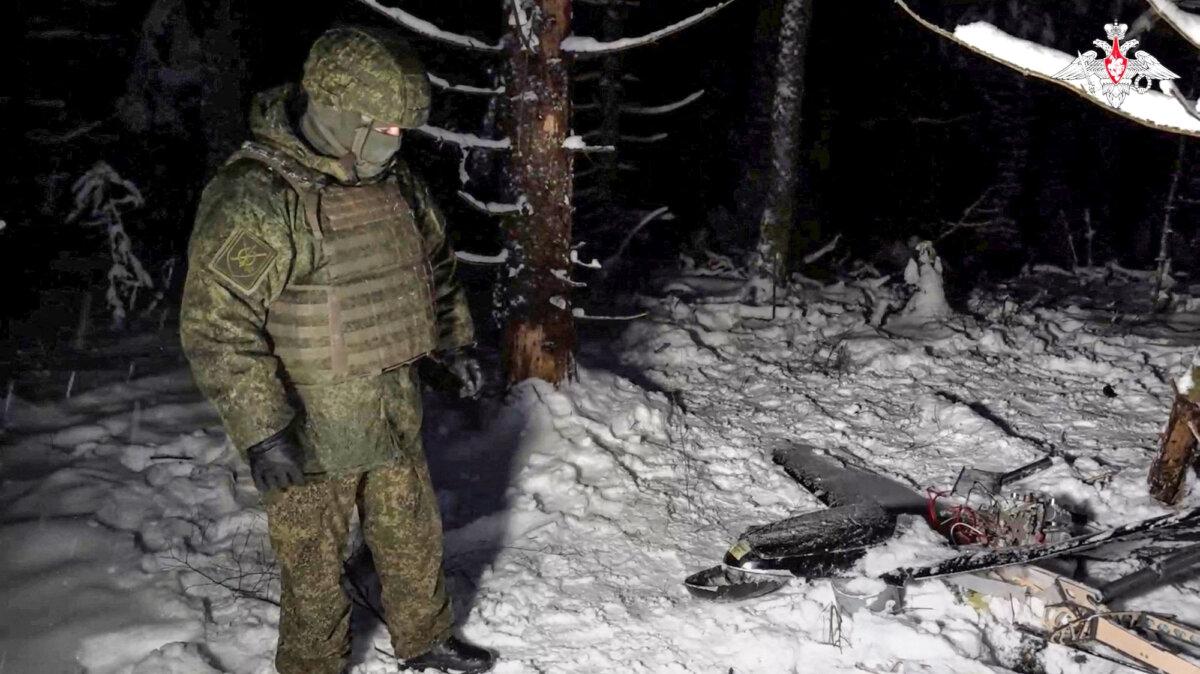 A Russian soldier stands next to the remains of a drone downed during an alleged Ukrainian attack on the Russian presidential residence in the Novgorod Region, Russia, in this still image from a video released on Dec. 31, 2025. (Russian Defence Ministry/Handout via Reuters)