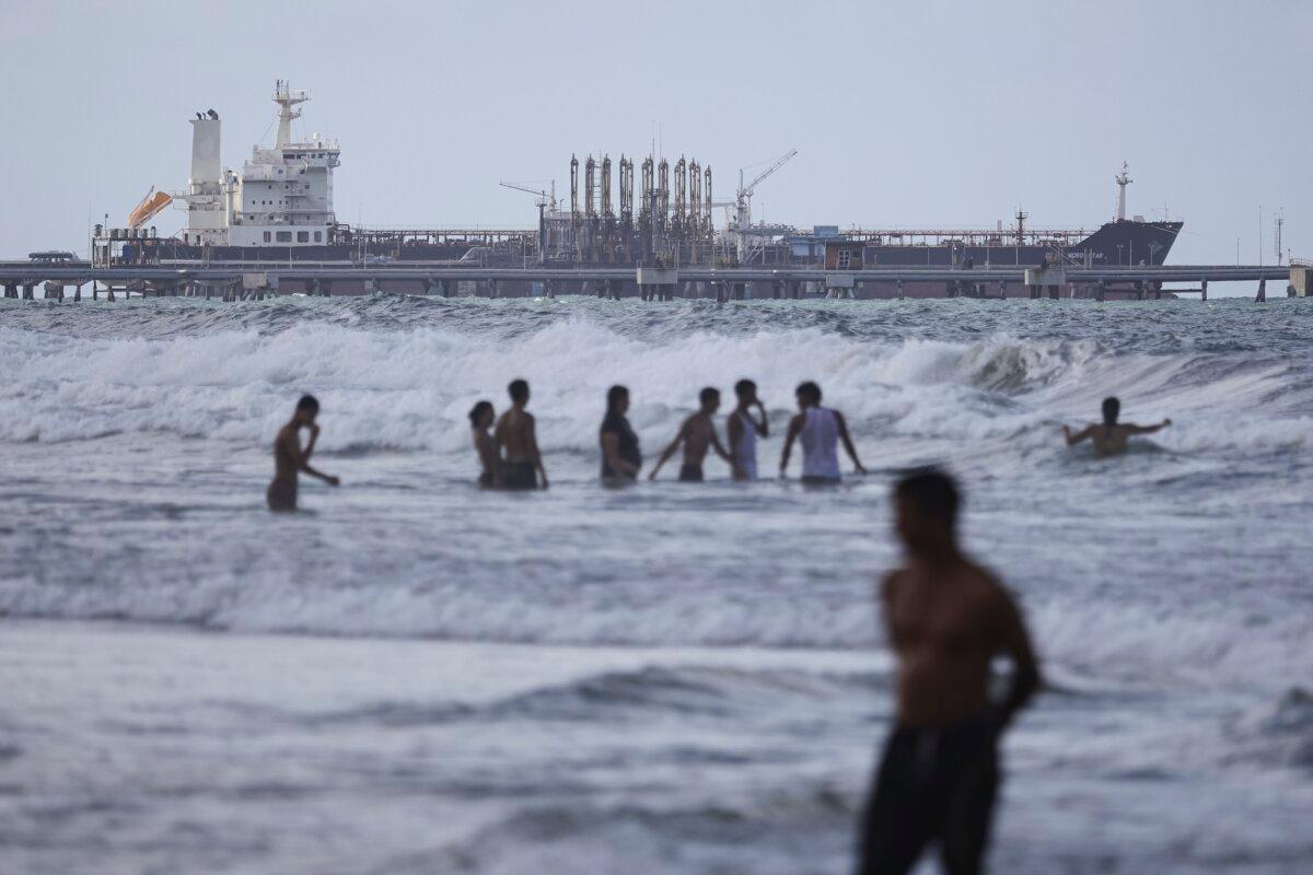 People walk on a beach in front of an oil tanker anchored at the dock near the El Palito refinery, in Puerto Cabello, Venezuela, on Dec. 18, 2025. (Jesus Vargas/Getty Images)