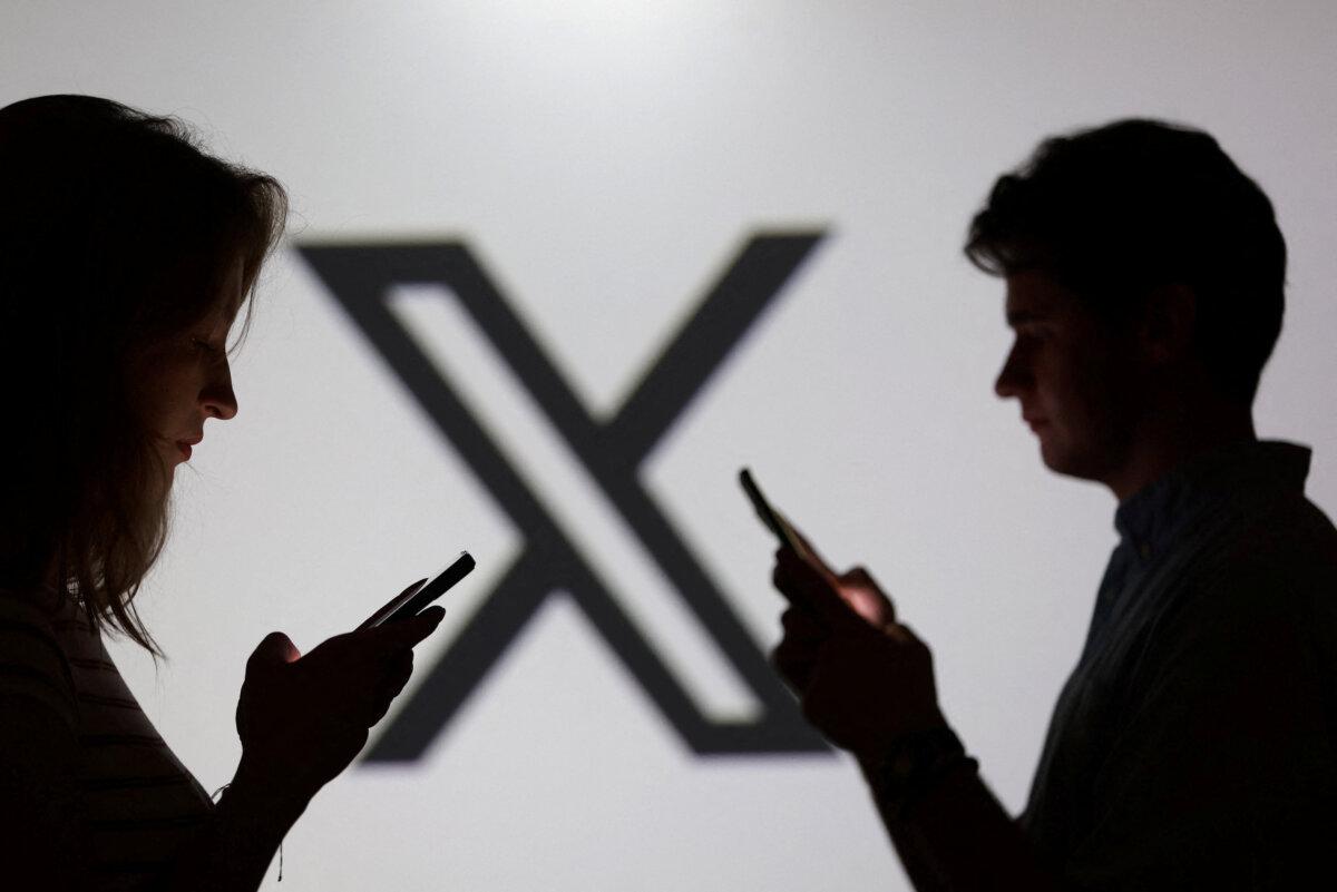 Teenagers pose for a photo while holding smartphones in front of a X logo in this illustration taken Sept. 11, 2025. (Dado Ruvic/Reuters)