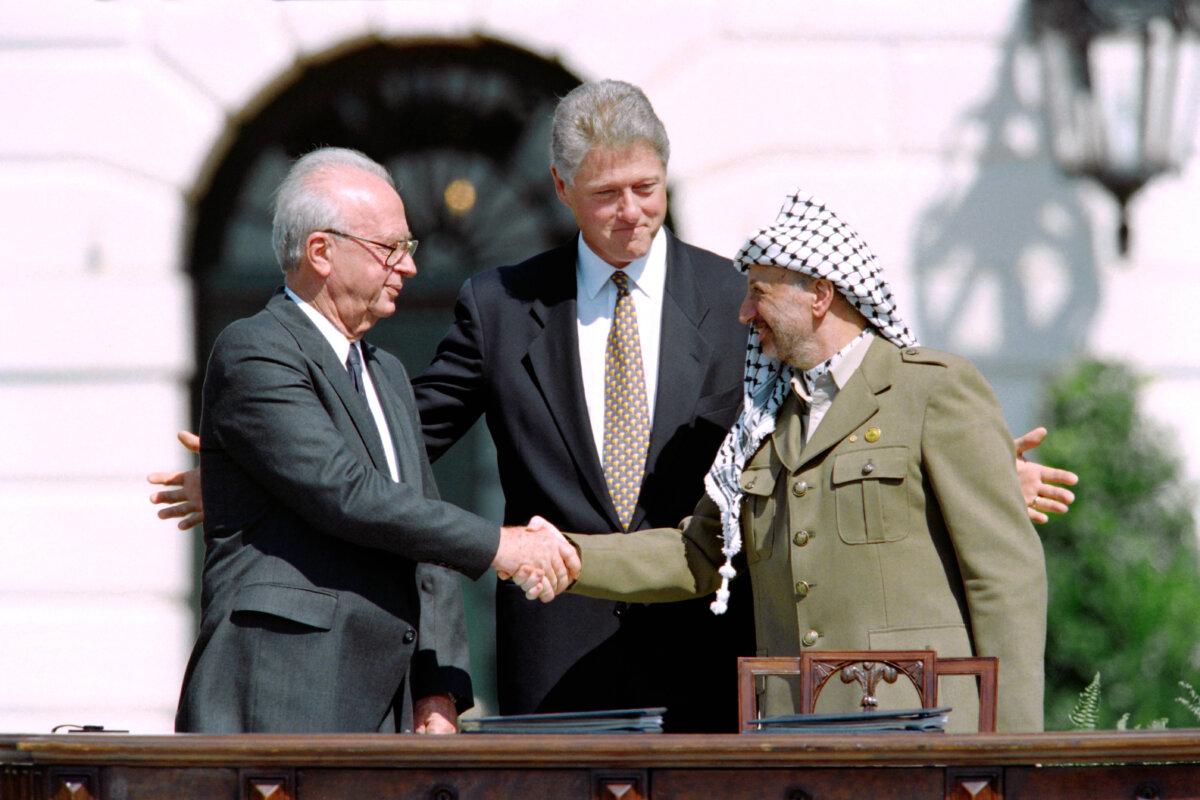 U.S. President Bill Clinton stands between PLO leader Yasser Arafat (R) and Israeli Prime Minister Yitzhak Rabin (L) as they shake hands for the first time, after signing the historic Israel–PLO Oslo Accords on Palestinian autonomy in the occupied territories, at the White House on Sept. 13, 1993. (J. David Ake/AFP via Getty Images)