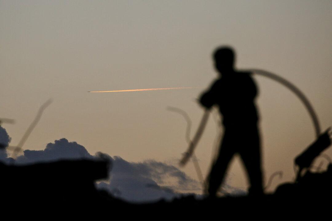 A person is silhouetted while standing on the rubble in the Bureij refugee camp in the central Gaza Strip as a plane flies in the background on February 3, 2026. Beginning in October, a fragile ceasefire has so far halted two years of war between Israel and Hamas in the Gaza Strip despite both sides trading accusations of truce violations. (Photo by Eyad BABA / AFP via Getty Images)