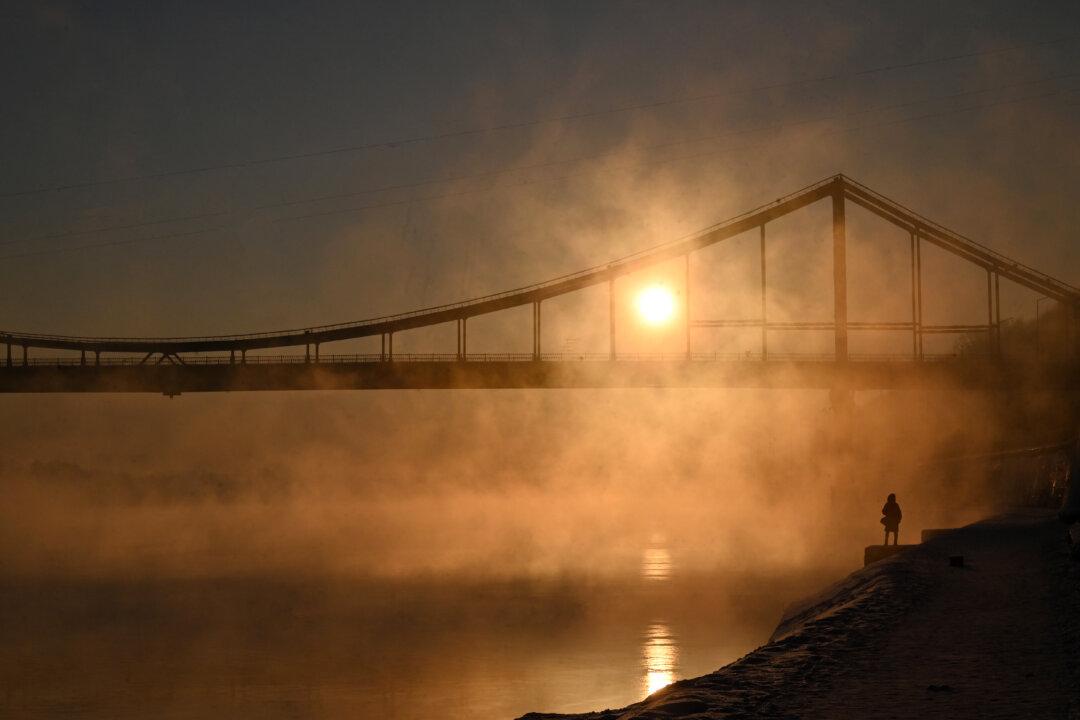A girl looks at the sun rising over the Dnipro River in Kyiv on February 4, 2026. (Photo by Sergei SUPINSKY / AFP via Getty Images)