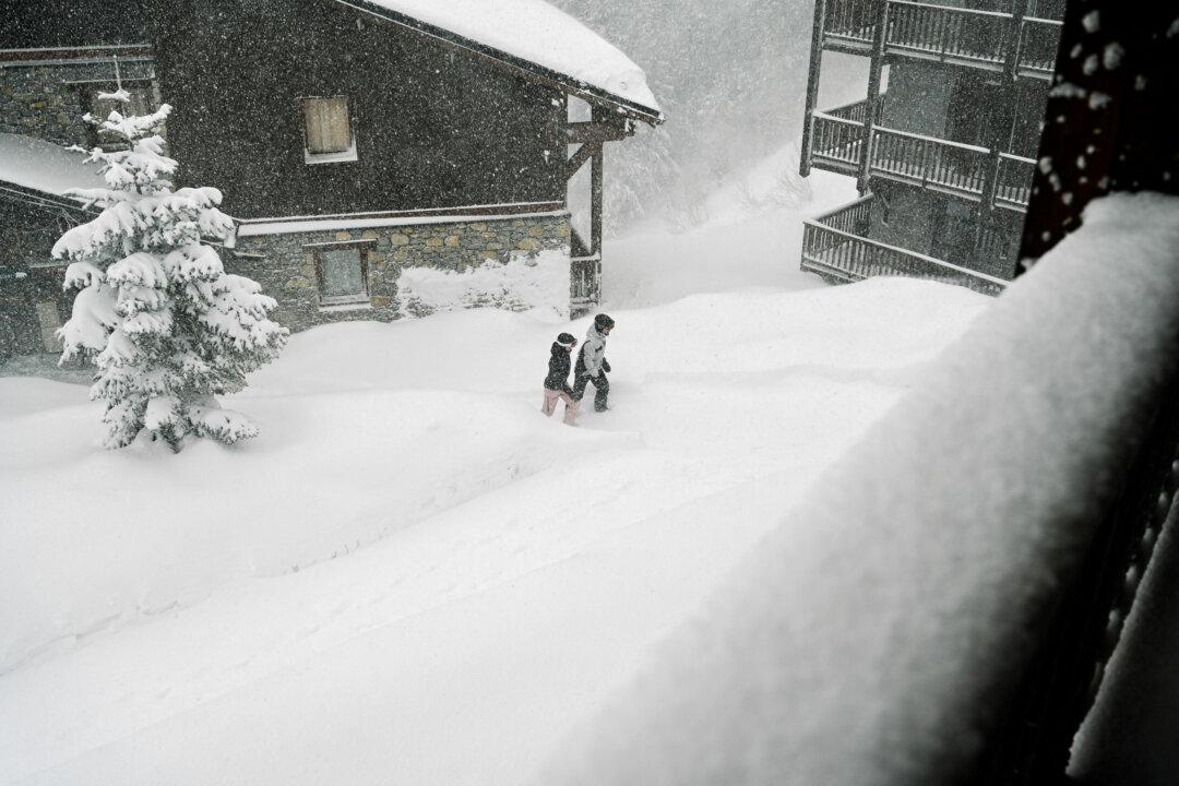 Two people walk through the snow among snow-covered mountain chalets during a period of heavy snowfall at the Arc 2000 ski resort in Bourg Saint Maurice in France on February 11 2026. (Photo by Matthieu Delaty / Hans Lucas / AFP via Getty Images)