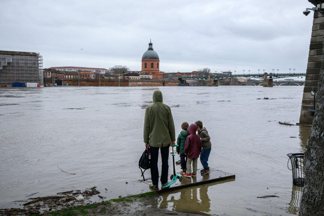 People stand before the elevated water level of the Garonne river following heavy rainfall, in Toulouse, southwestern France on February 11, 2026. Seventeen departments, from the Atlantic coast to the Massif Central, are on orange alert on February 11, 2026 at midday as Storm Nils approaches, while six others are on alert for strong winds in Corsica and avalanches in the Alps. (Photo by Ed JONES / AFP via Getty Images)