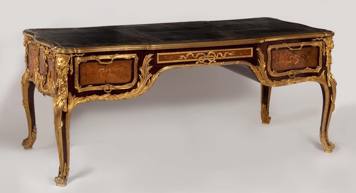 Writing table, 1786, by Guillaume Beneman. oak, purpleheart, sycamore, ebony, boxwood, casuarina, gilt-bronze, leather; 35 1/4 inches by 74 3/4 inches by 31 inches. This desk replaced the 1759 red-lacquered oak writing table (bureau plat) made by Gilles Joubert. Waddesdon Manor, England. (Public Domain)