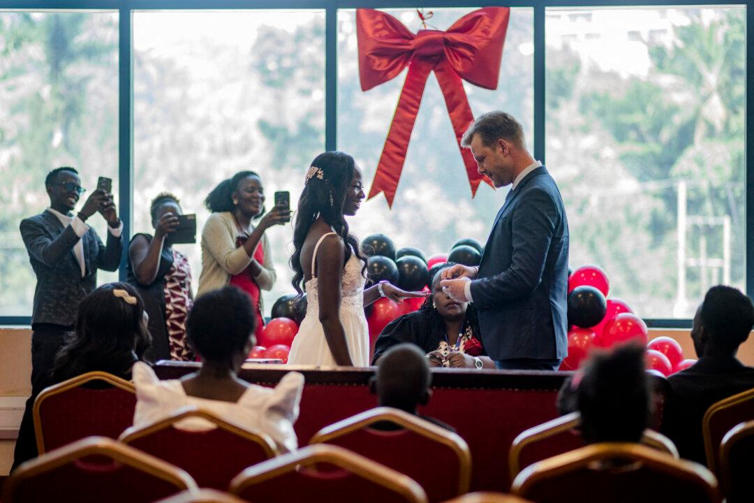 TOPSHOT - Couples exchange vows and rings in a ceremony led by a commissioner for Civil Registration at the National Identification and Registration Authority (NIRA) in Kampala, Uganda, on February 13, 2026. Fourteen couples, representing Ugandans, Congolese, and Eritreans, participated in a special Valentine's Day event organized by NIRA. Although many couples preferred to marry on the actual Valentine's Day, the ceremony was held a day earlier due to NIRA's closure on Saturday. (Photo by BADRU KATUMBA / AFP via Getty Images)
