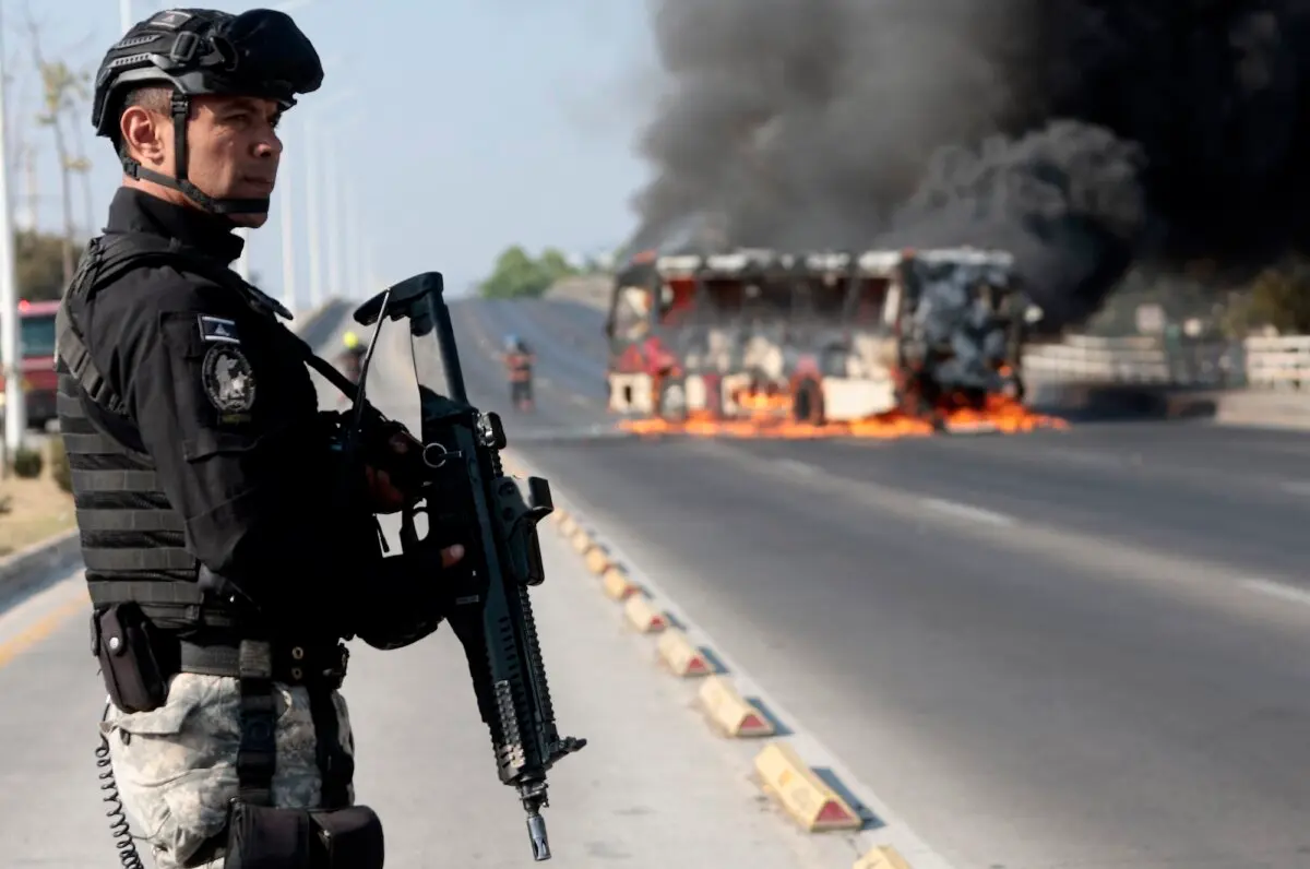 A member of the Prosecutor's Office stands guard near a burning bus at one of the main avenues after it was set on fire by organised crime groups in response to an operation in Jalisco to arrest a high-priority security target in Zapopan, state of Jalisco, Mexico, on Feb. 22, 2026. (Ulises Ruiz/AFP)