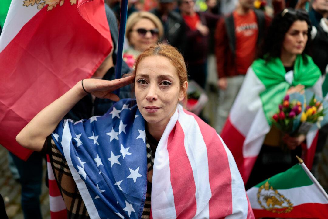 EDINBURGH, SCOTLAND - MARCH 05: A woman gives a salute gesture while wearing a US flas as Iranians pose with flags and posters outside the U.S. Consulate on March 05, 2026 in Edinburgh, Scotland. Iran's Supreme Leader, Ayatollah Ali Khamenei, was confirmed killed after the United States and Israel launched a joint attack on Iran on February 28. Iran retaliated by firing waves of missiles and drones at Israel, and targeting U.S. allies in the region. (Photo by Jeff J Mitchell/Getty Images)