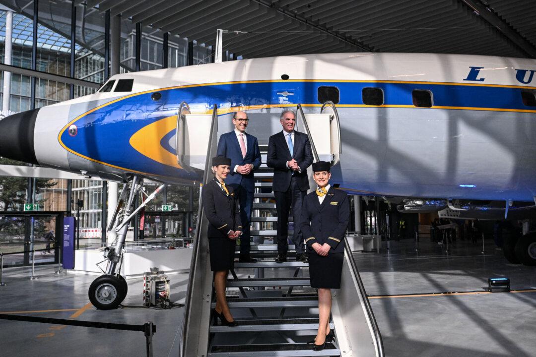 The CEO of German airline Lufthansa Carsten Spohr (top R) and Lufthansa CFO Till Streichert pose with flight attendants on the stairs of a historic Lufthansa plane before their press conference to present the company's 2025 results in Frankfurt am Main, Germany, on March 6, 2026. (Kirill Kudryavtsev / AFP via Getty Images)