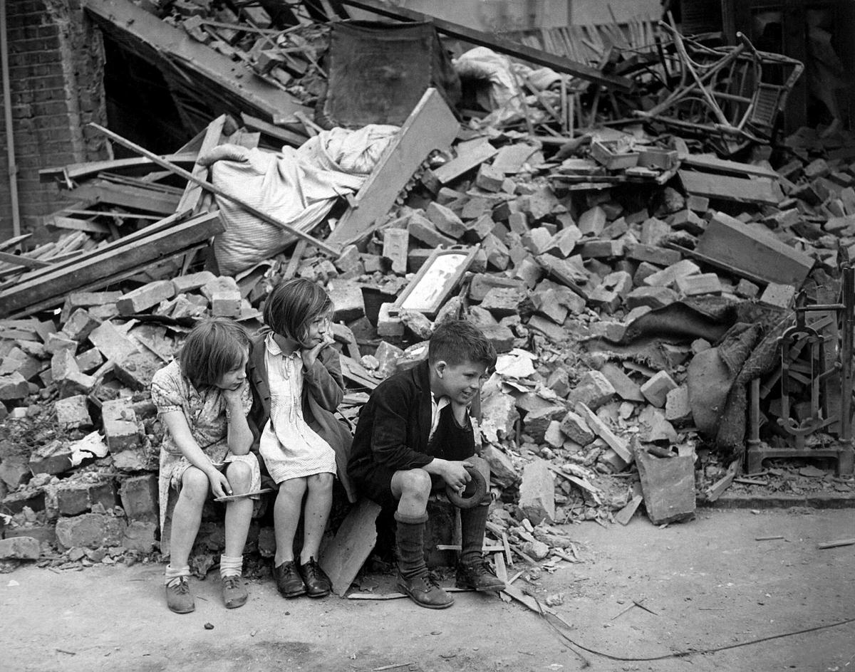 Children wait outside the wreckage of what was once their home, in East London, 1940. (<a href="https://en.wikipedia.org/wiki/User:Sue_Wallace">Sue Wallace</a>/<a href="https://creativecommons.org/licenses/by-sa/2.0/deed.en">CC BY-SA 2.0</a>)