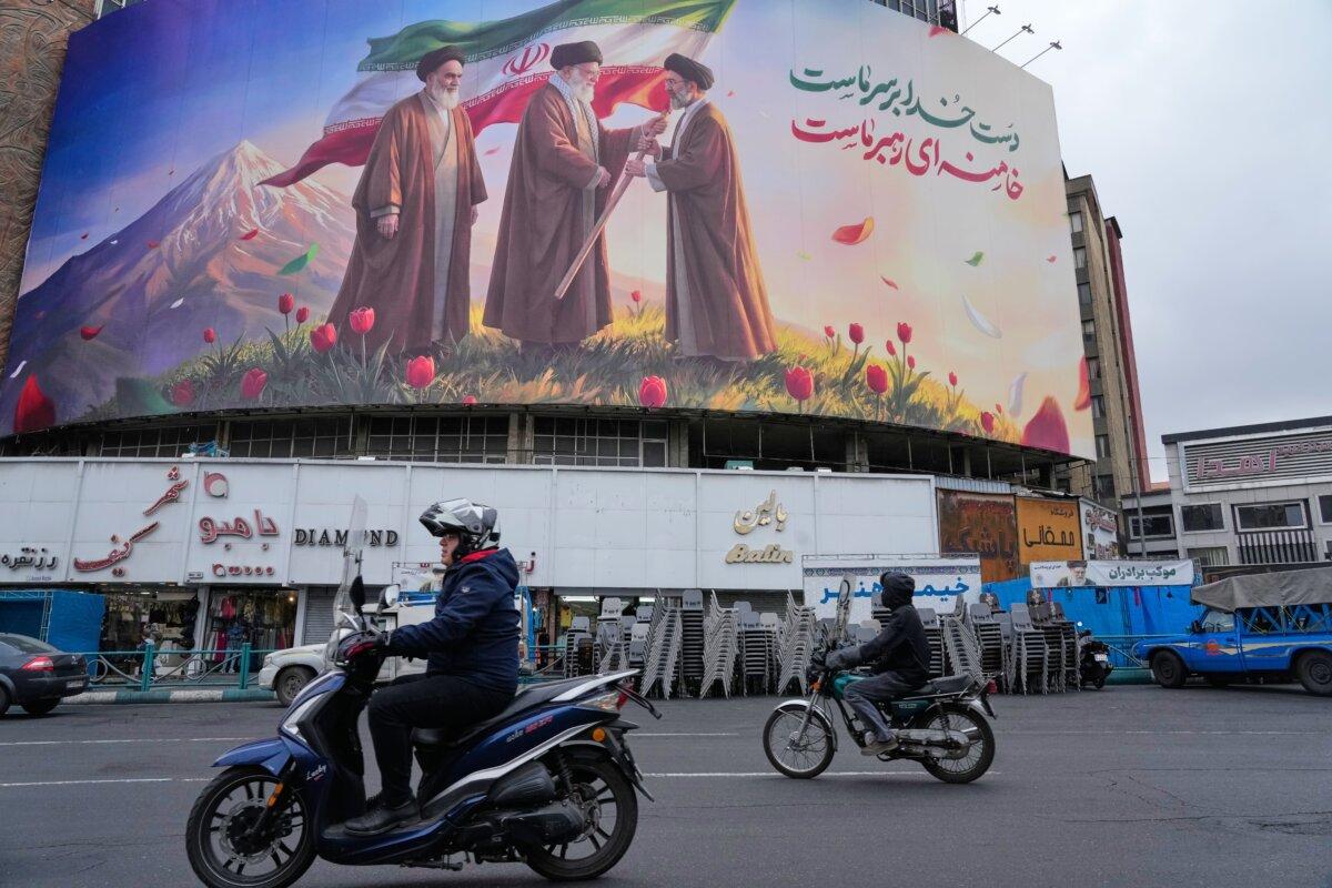 Motorbikes drive past a billboard depicting Iran’s late Supreme Leader Ayatollah Ali Khamenei (C) handing the country’s flag to his son and successor Ayatollah Mojtaba Khamenei (R), as the late revolutionary founder Ayatollah Ruhollah Khomeini (L) watches, in a square in downtown Tehran, Iran, on March 10, 2026. (Vahid Salemi/AP Photo)