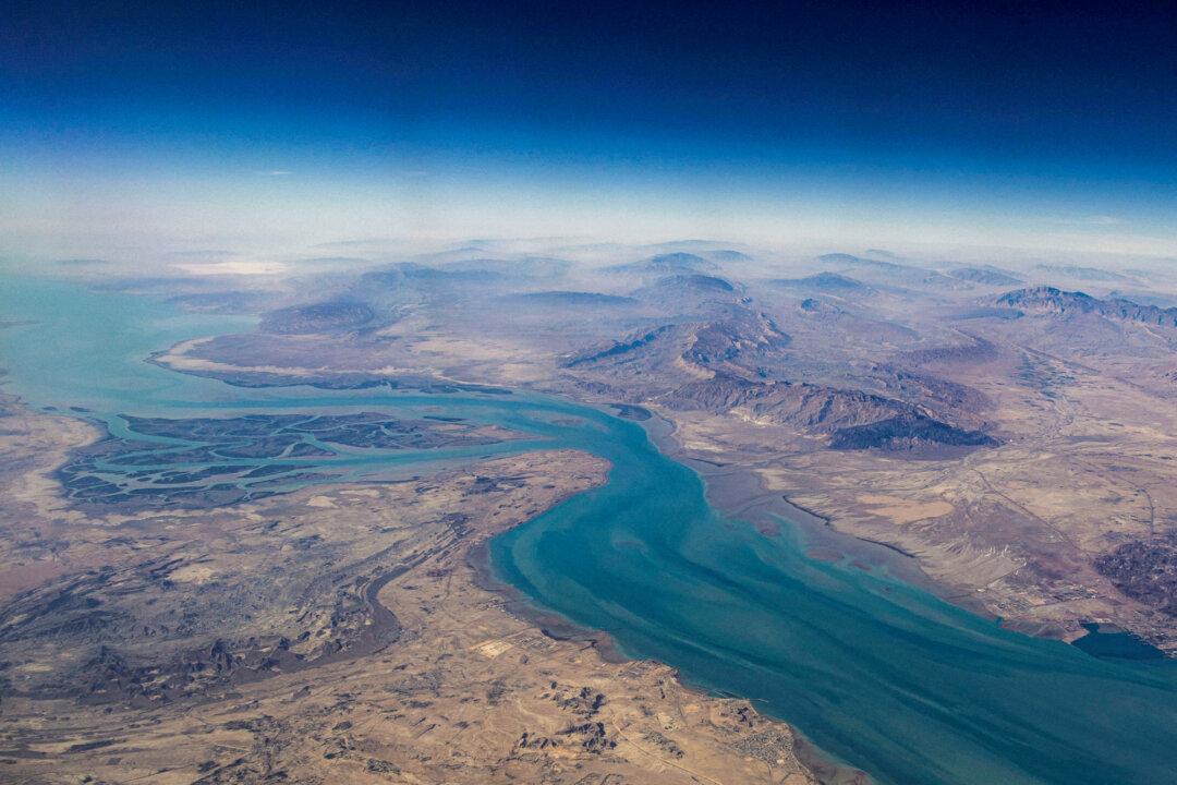 (Top) Tankers sail in the Gulf, near the Strait of Hormuz, amid the U.S.–Israeili war with Iran as seen from northern Ras al-Khaimah, near the border with Oman’s Musandam governance, in the United Arab Emirates on March 11, 2026. (Bottom) An aerial view of the island of Qeshm, separated from the Iranian mainland by the Clarence Strait, in the Strait of Hormuz, on Dec. 10, 2023. (Stringer/File Photo/Reuters)
