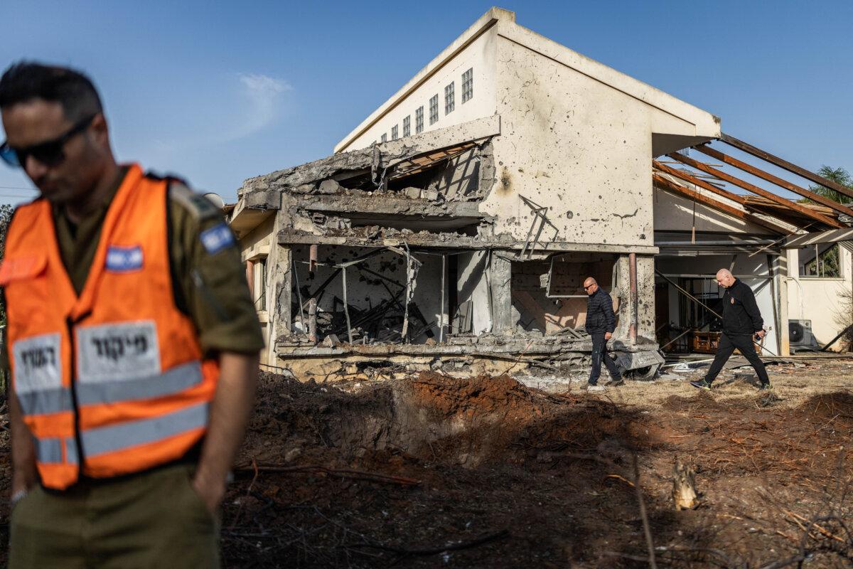 A member of the Home Front Command (L) stands next to a damaged house that was hit by a rocket reportedly fired by the Tehran-backed Hezbollah terrorist group in Haniel, Israel, on March 12, 2026. (Ilia Yefimovich/AFP via Getty Images) /