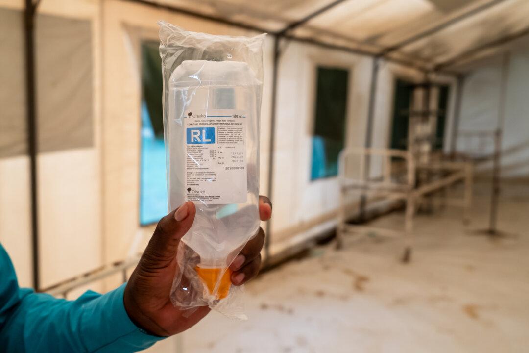 (Top) Senior Health Surveillance Assistant Robert Amissi sits near medical records outside Monkey Bay, Malawi, on Feb. 18, 2026. (Bottom Left) Lactated intravenous infusion solution used to treat cholera sits in an isolation area at a clinic outside Monkey Bay, Malawi, on Feb. 18, 2026. The treatment helps restore hydration and correct metabolic acidosis. (Bottom Right) A cholera isolation area awaits patients outside Monkey Bay, Malawi, on Feb. 18, 2026. (John Fredricks/The Epoch Times)
