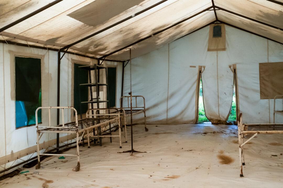(Top) Senior Health Surveillance Assistant Robert Amissi sits near medical records outside Monkey Bay, Malawi, on Feb. 18, 2026. (Bottom Left) Lactated intravenous infusion solution used to treat cholera sits in an isolation area at a clinic outside Monkey Bay, Malawi, on Feb. 18, 2026. The treatment helps restore hydration and correct metabolic acidosis. (Bottom Right) A cholera isolation area awaits patients outside Monkey Bay, Malawi, on Feb. 18, 2026. (John Fredricks/The Epoch Times)