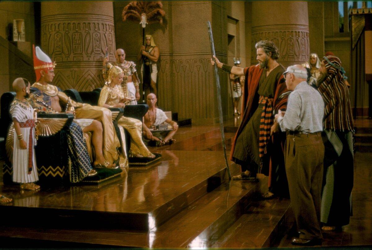 (L–R) Eugene Mazzola, Yul Brynner, Anne Baxter, Charlton Heston, director Cecil B. DeMille, and John Carradine on the set of “The Ten Commandments.” (Paramount Pictures)