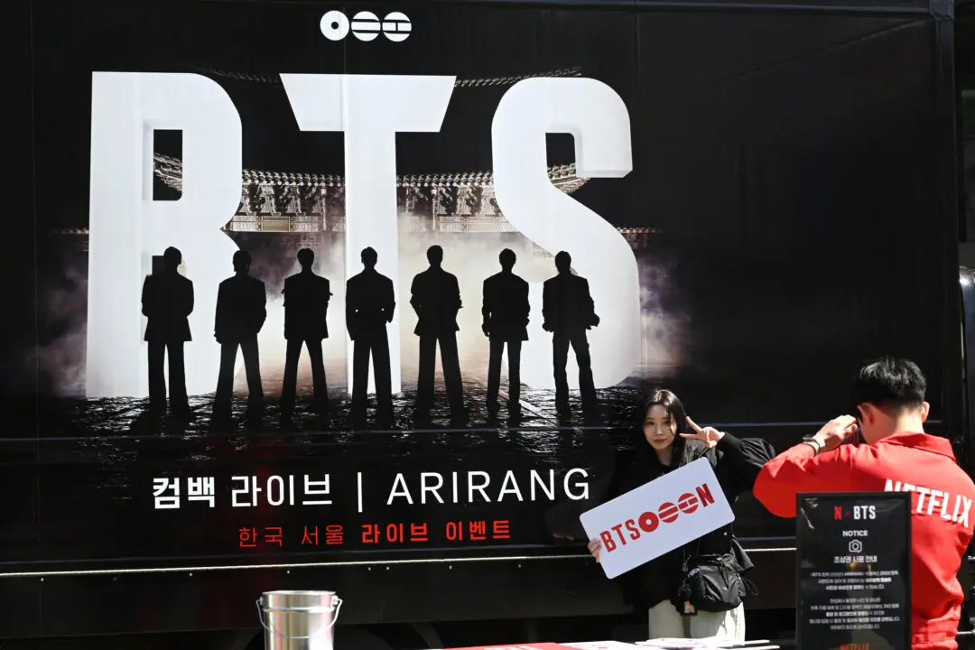 A woman poses for a photo in front of a truck promoting the comeback concert of K-pop boy group BTS in Seoul on March 19, 2026. BTS, the world's biggest boy band, reunites on stage on March 21, in a K-pop extravaganza watched by hundreds of thousands of fans in downtown Seoul and by millions around the planet online. (Photo by Jung Yeon-je / AFP via Getty Images)
