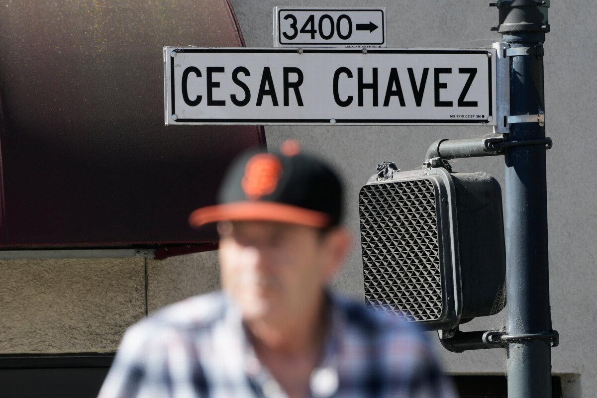 A pedestrian walks below a Cesar Chavez Street sign in San Francisco on March 18, 2026. (AP Photo/Jeff Chiu)