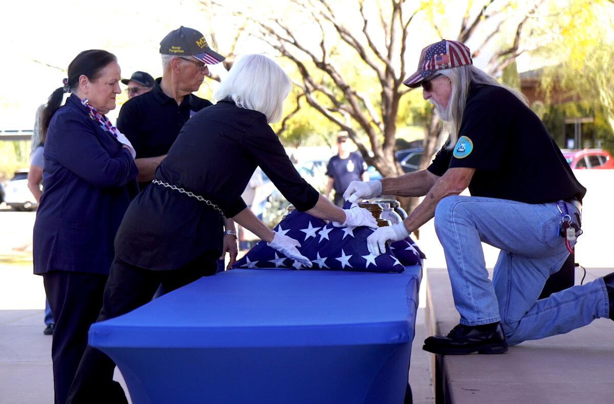 A volunteer arranges folded flags beside 15 cremation remains during an interment service at the National Memorial Cemetery of Arizona in Phoenix on March 18, 2026. (Allan Stein/The Epoch Times)