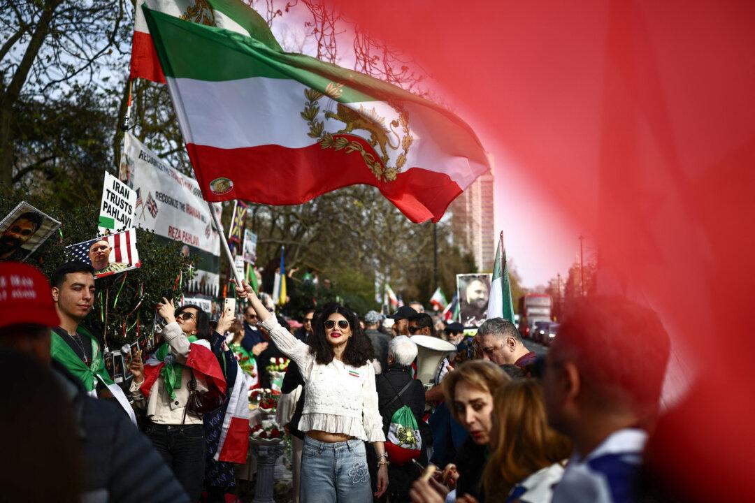 TOPSHOT - An anti-Iranian regime protester waves an Iranian flags before the 1979 revolution with the Lion and Sun emblem at a protest, outside the Iranian Embassy in central London on March 20, 2026. (Photo by Henry NICHOLLS / AFP via Getty Images)