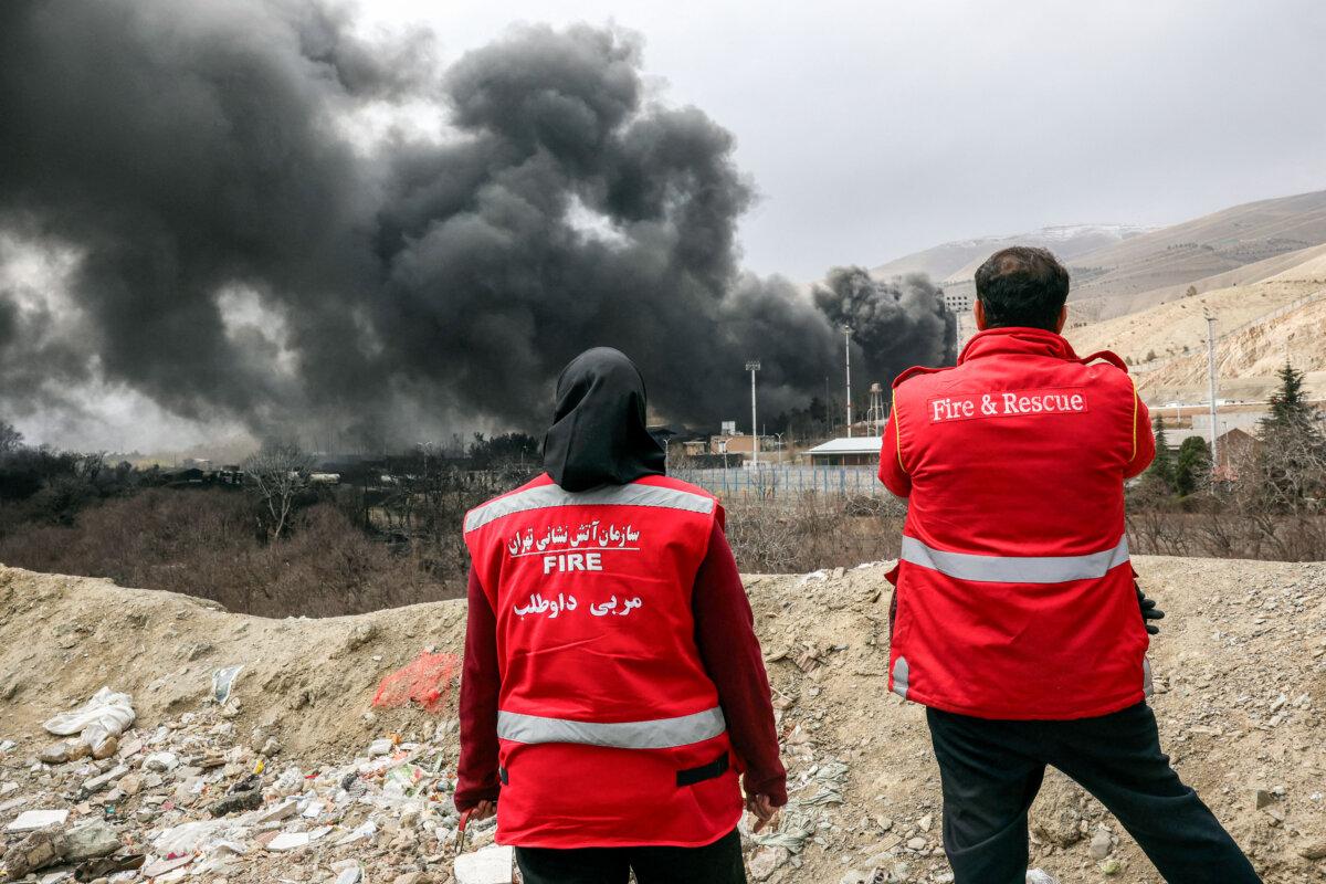 Iranian civil defense members watch smoke plumes rise from an ongoing fire following an overnight air strike on the Shahran oil refinery in northwestern Tehran, Iran, on March 8, 2026. (AFP via Getty Images)