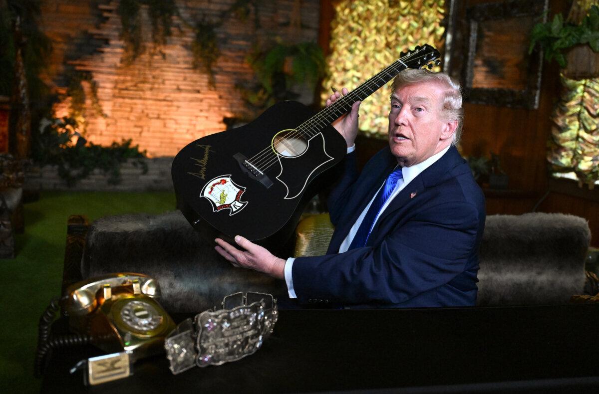 President Donald Trump holds up a replica of an Elvis Presley guitar after signing it while visiting Graceland, the Presley's home in Memphis, Tenn., on March 23, 2026. (Roberto Schmidt/Getty Images)