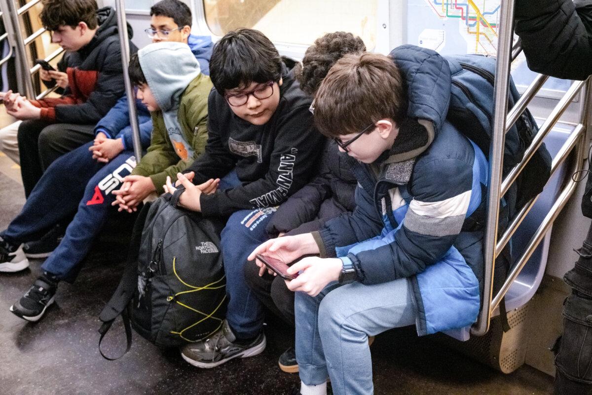 Boys look at a phone on a subway in New York City on March 26, 2026. (Samira Bouaou/The Epoch Times)