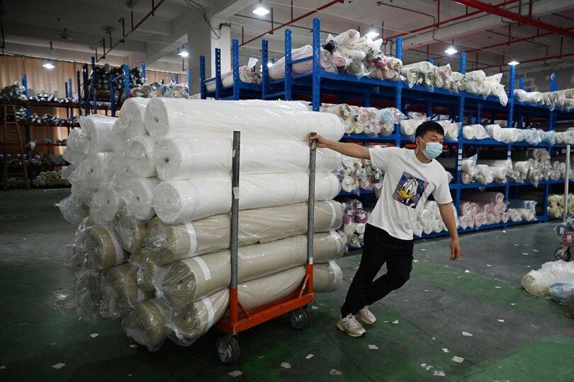 A worker hauls rolls of fabric after unloading them at a warehouse in a textile industrial park in Shaoxing, Zhejiang Province, China, on May 9, 2025. (Greg Baker/AFP via Getty Images)