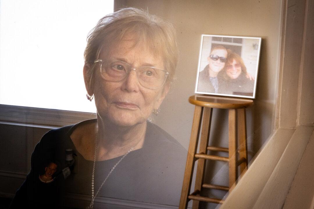 Judy Rogg is reflected in a window with a photo of her and her late son Erik in the background in Los Angeles on April 15, 2026. Rogg hopes lawsuits and legislation will eventually lead to change, but thinks education is the missing link. (John Fredricks/The Epoch Times)
