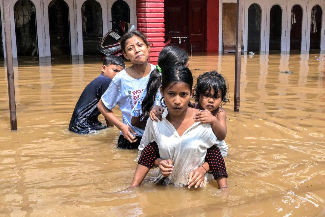 TOPSHOT - Children wade through floodwaters following heavy rainfall in Guwahati on April 20, 2026. (Photo by Biju BORO / AFP via Getty Images)